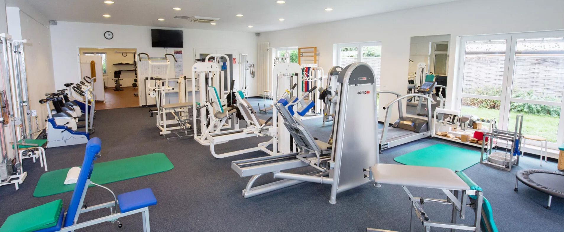 Innenraum eines Fitnessstudios mit verschiedenen Trainingsgeräten und großen Fenstern